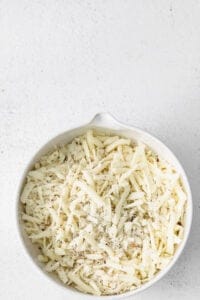 shredded cheese in a white bowl on a white background.