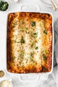 lasagna in a white baking dish with parmesan cheese and herbs.
