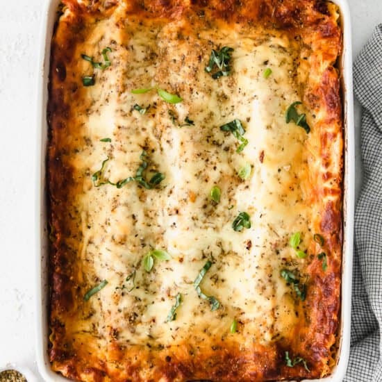 lasagna in a white baking dish with parmesan cheese and herbs.