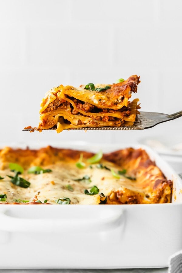 a slice of lasagna being taken out of a baking dish.