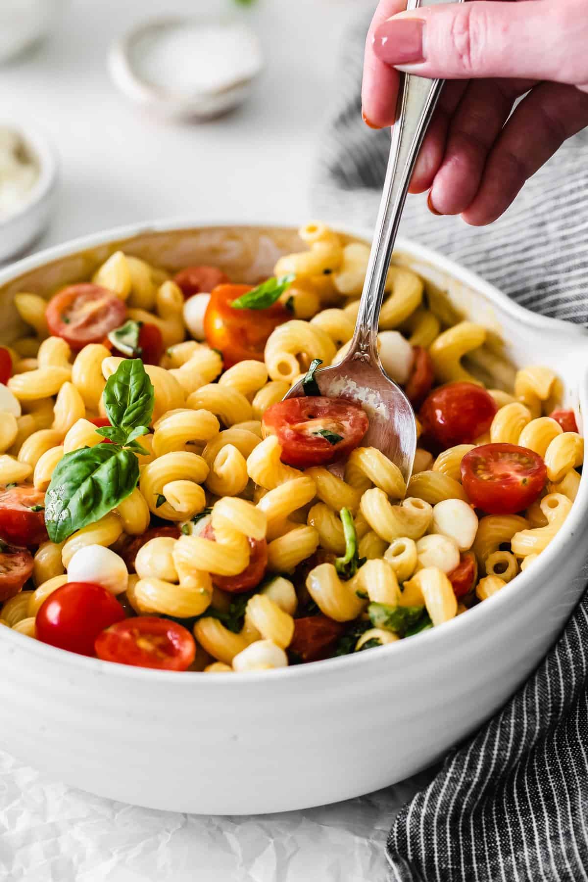 A spoon taking a scoop of Caprese pasta salad. 