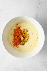 a bowl of soup with carrots and nuts in it.