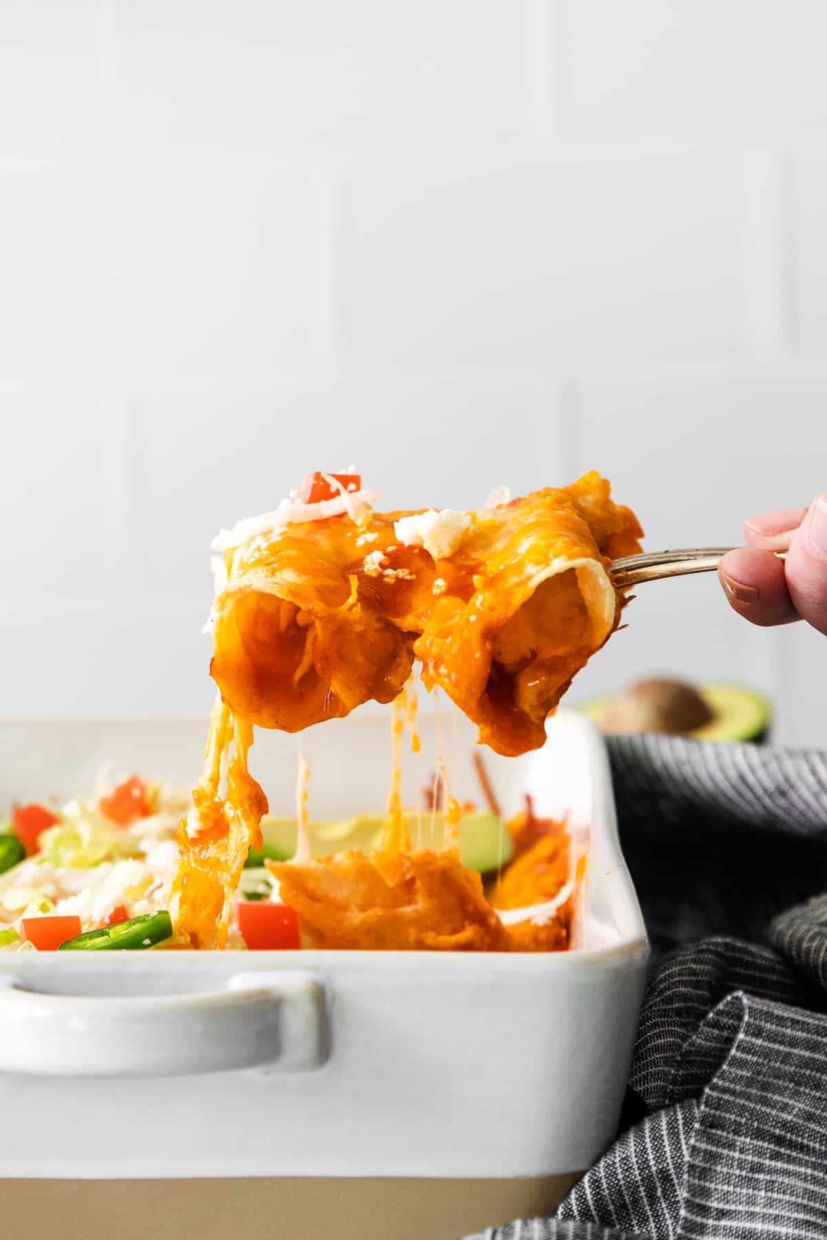 Cheese enchiladas being scooped out of a casserole dish.