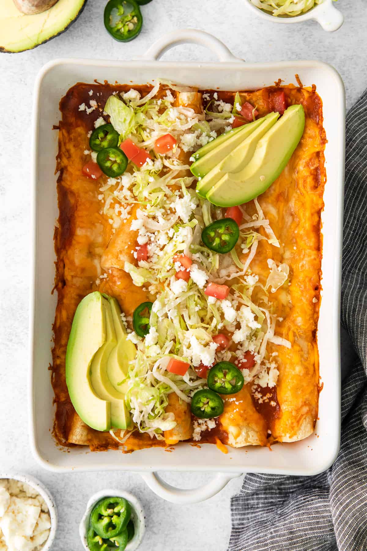 Cheese enchiladas garnished with toppings in a casserole dish.