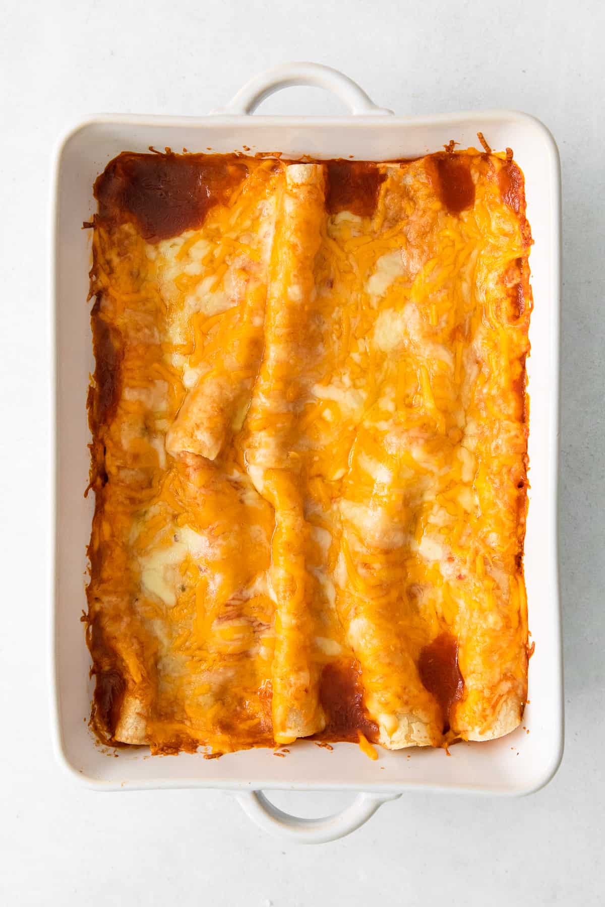 Cheese enchiladas baked in a casserole dish.