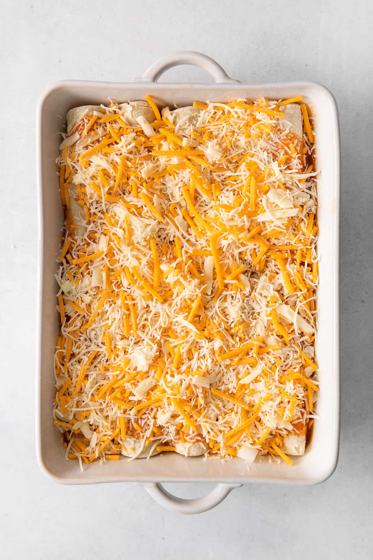 Enchiladas covered in shredded cheese in a casserole dish.