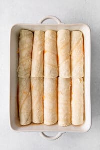 a white baking dish filled with rolled up burritos.