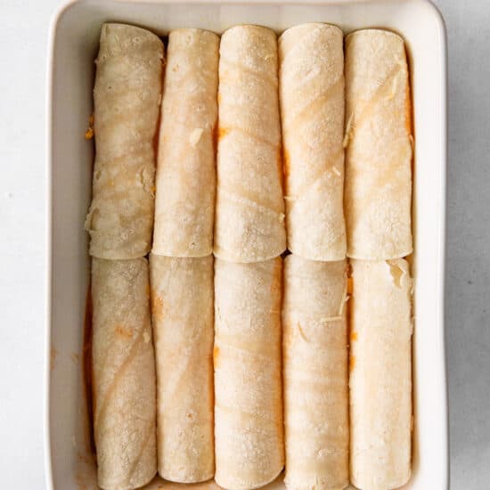 a white baking dish filled with rolled up burritos.