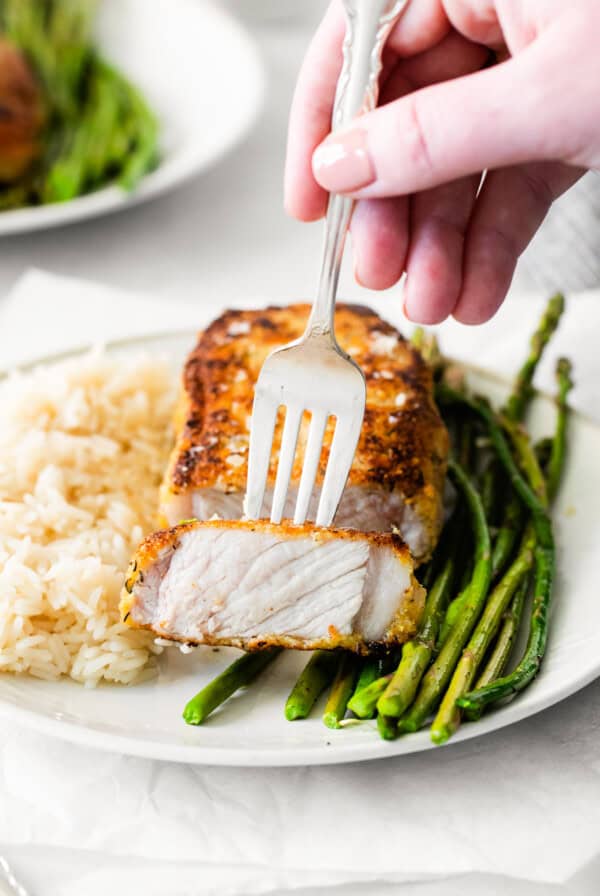 A fork holding a piece of parmesan crusted pork.