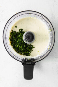 a food processor filled with white sauce and herbs.