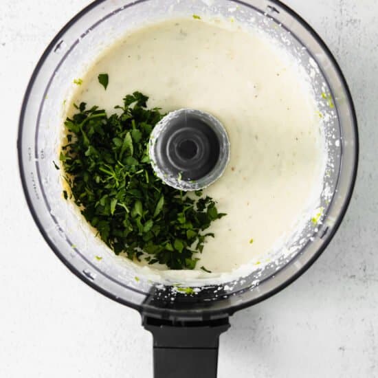 a food processor filled with white sauce and herbs.