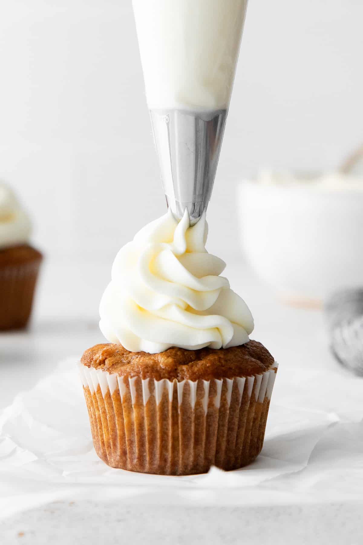 piping cream cheese frosting onto cupcake.