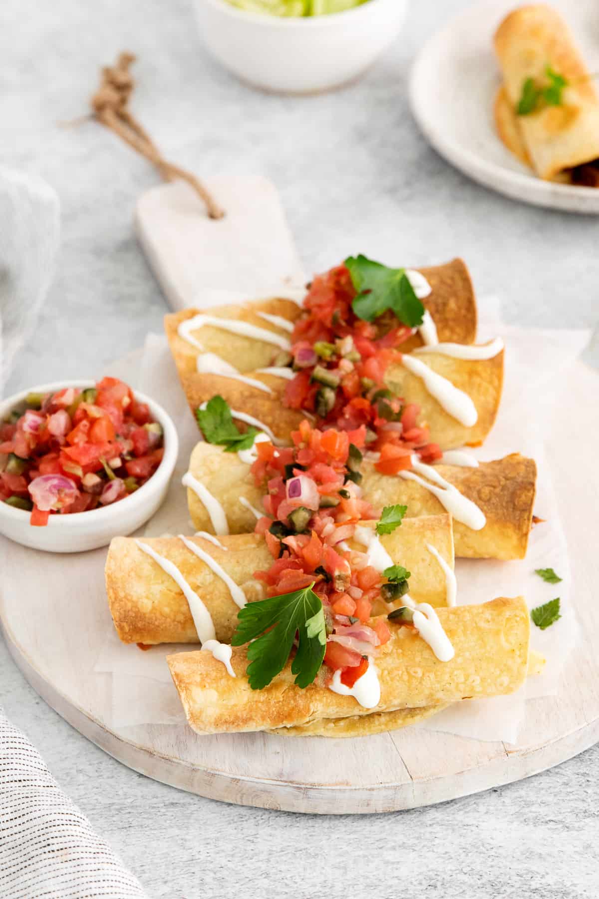 Taquitos topped with pico de gallo on a cutting board.
