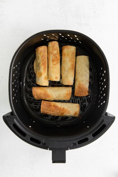 a black air fryer with a bunch of spring rolls in it.