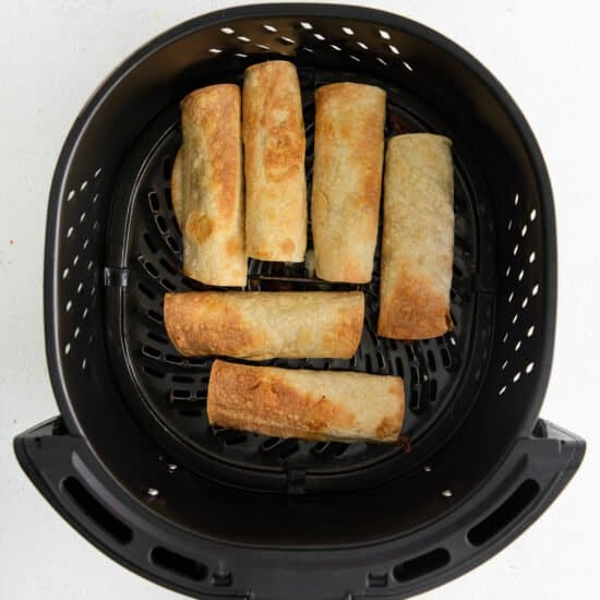 a black air fryer with a bunch of spring rolls in it.