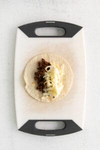 a taco with cheese and meat on a cutting board.