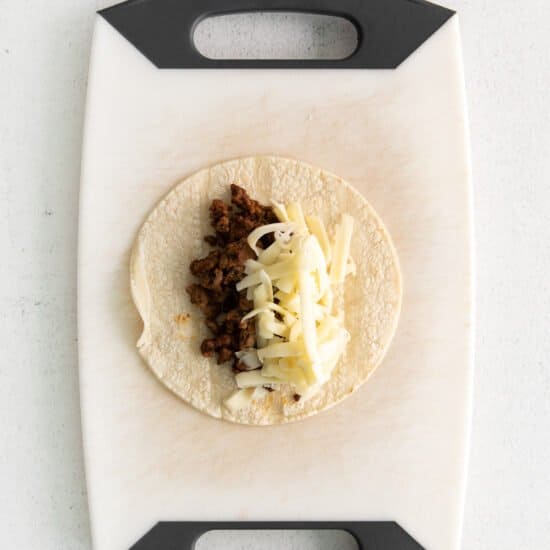 a taco with cheese and meat on a cutting board.