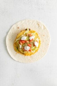 a tortilla filled with vegetables and cheese on a white background.