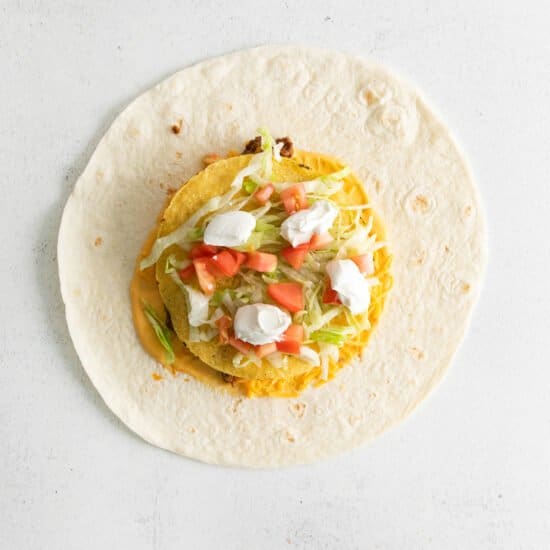 a tortilla filled with vegetables and cheese on a white background.