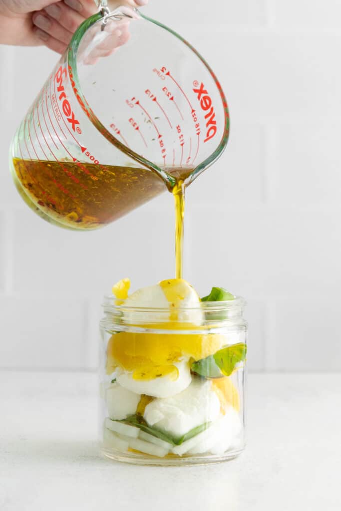 Pouring olive oil into a jar with goat cheese.