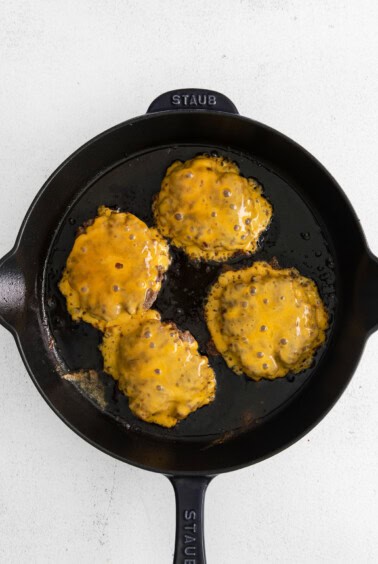 fried cheeseburgers in a skillet on a white background.