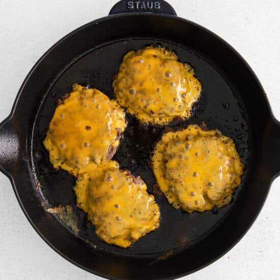 fried cheeseburgers in a skillet on a white background.