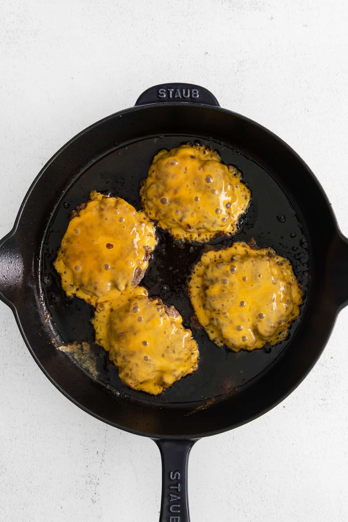 Cheeseburger patties in a cast iron skillet.