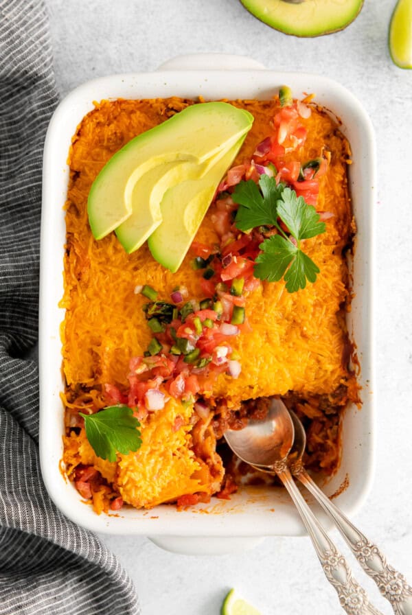 Beef taco bake in a white dish topped with avocado.