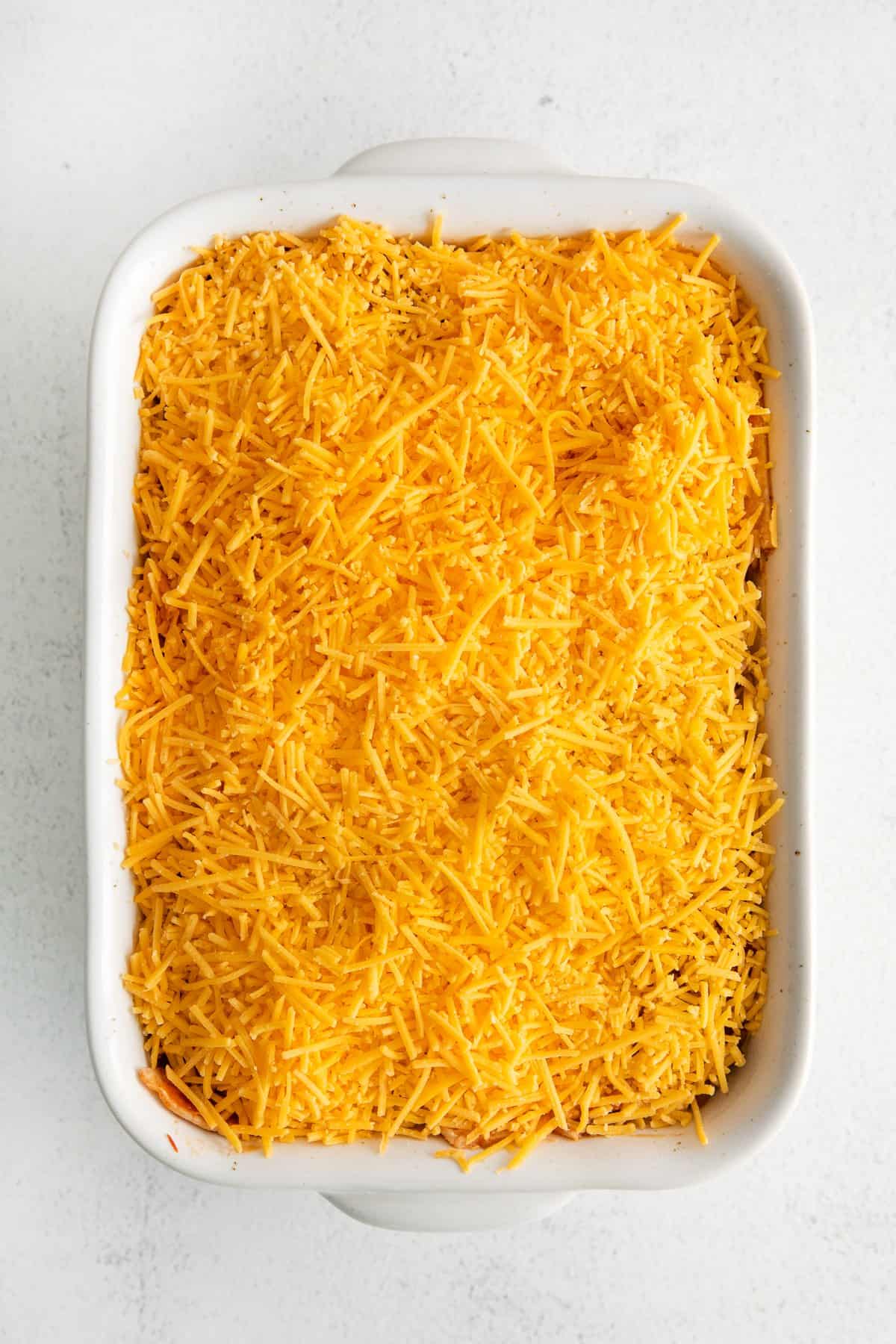 Taco bake in a casserole dish topped with shredded cheddar cheese.