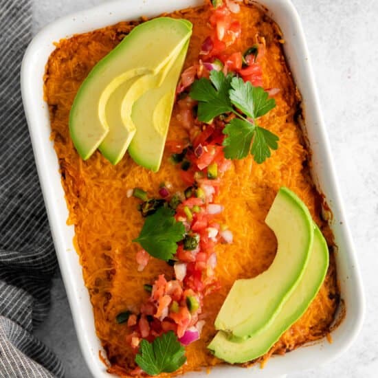 a white baking dish with a baked sweet potato casserole topped with avocado and cilantro.