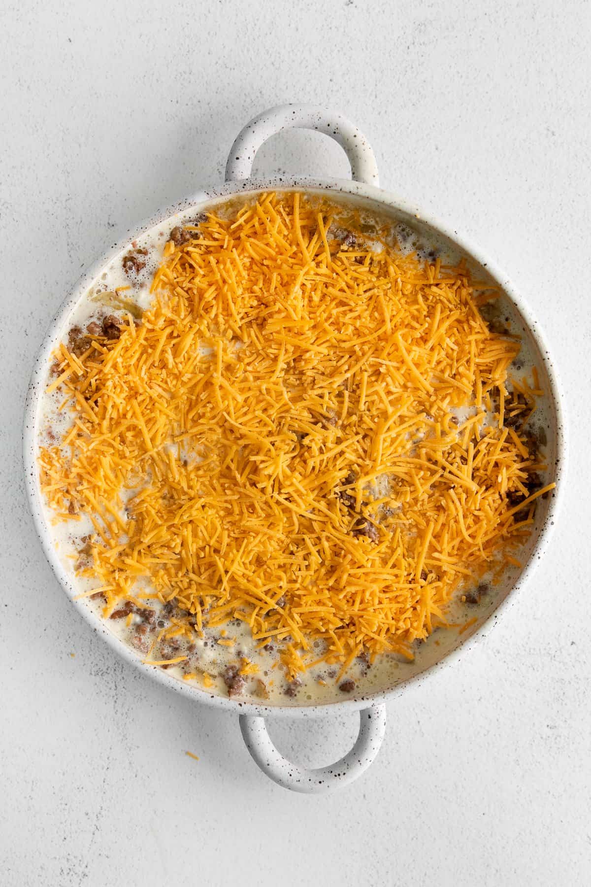 Cheeseburger pi in a baking dish topped with cheddar cheese. 
