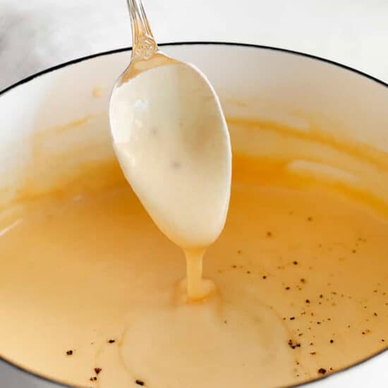 A spoon is pouring a sauce into a pot.