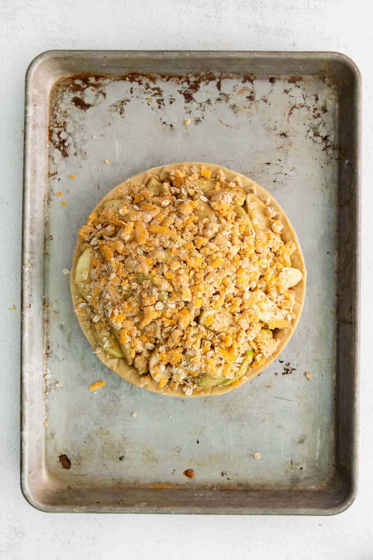 Crumble topping ready to be baked with an apple pie with cheese.