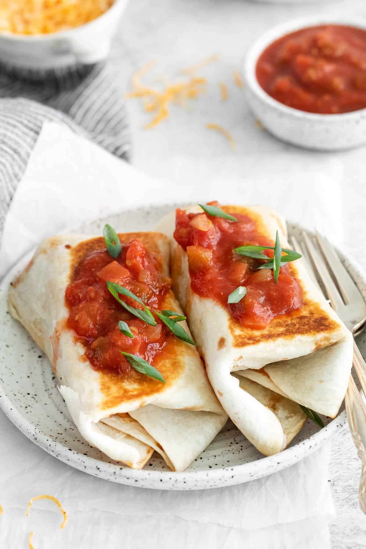 Bean and cheese burritos topped with salsa on a plate.