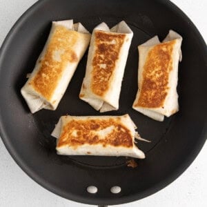 four tortillas in a frying pan on a white surface.