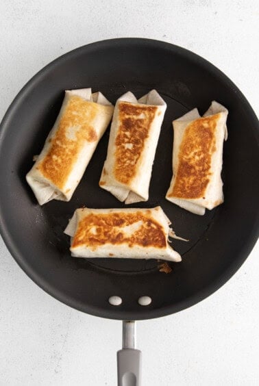 four tortillas in a frying pan on a white surface.