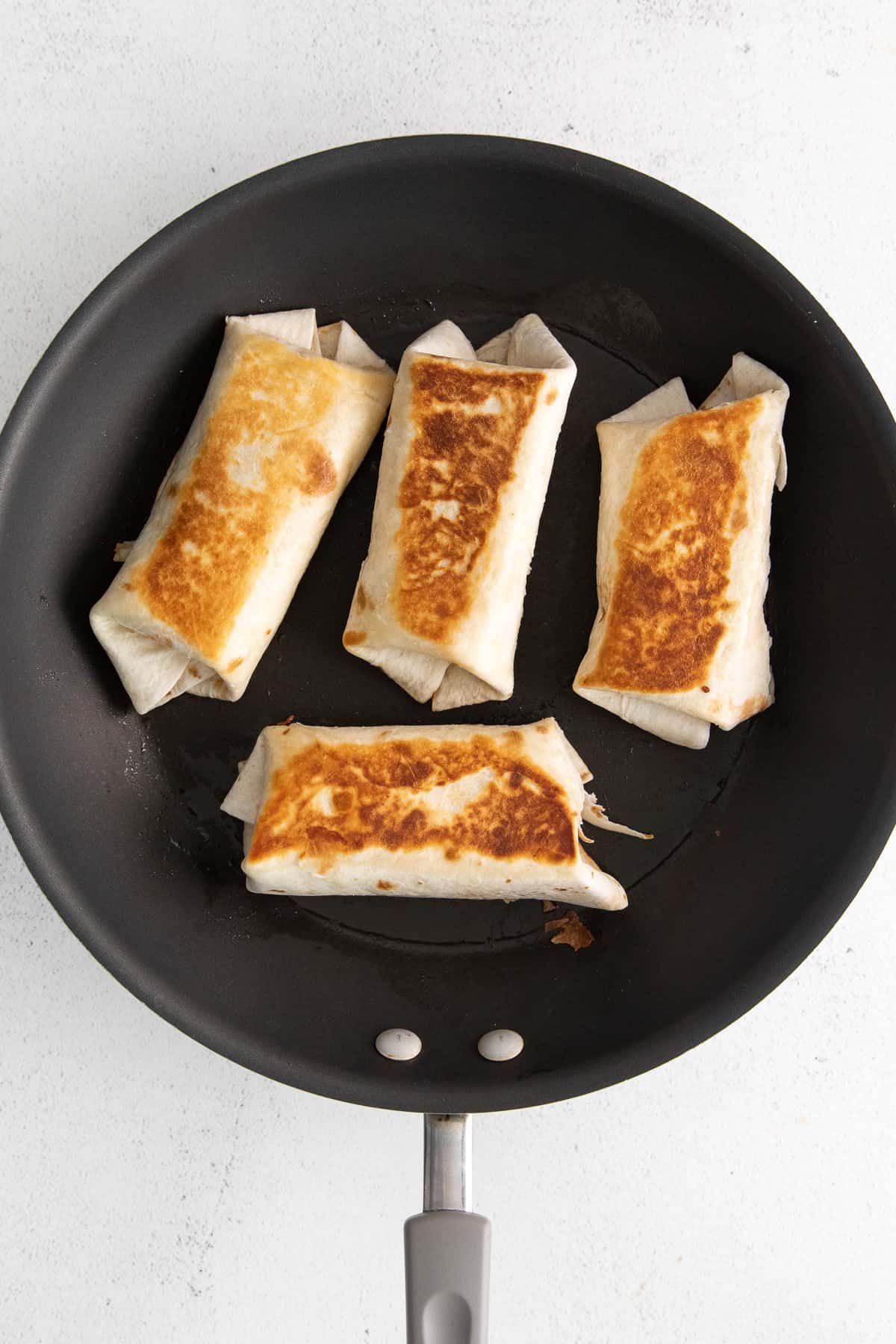 Bean and cheese burritos seared in a skillet.