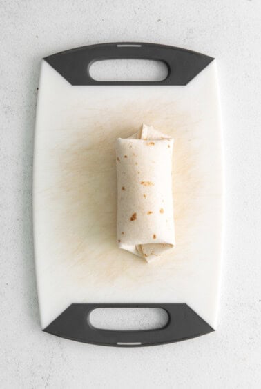 a burrito on a cutting board.
