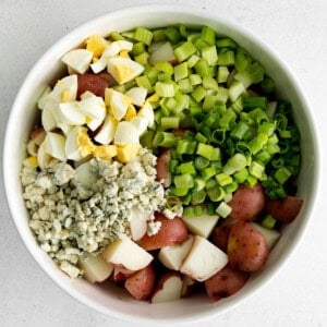 a white bowl filled with potatoes, eggs and green onions.