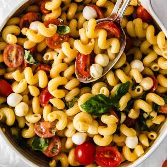 a bowl of pasta salad with tomatoes and basil.