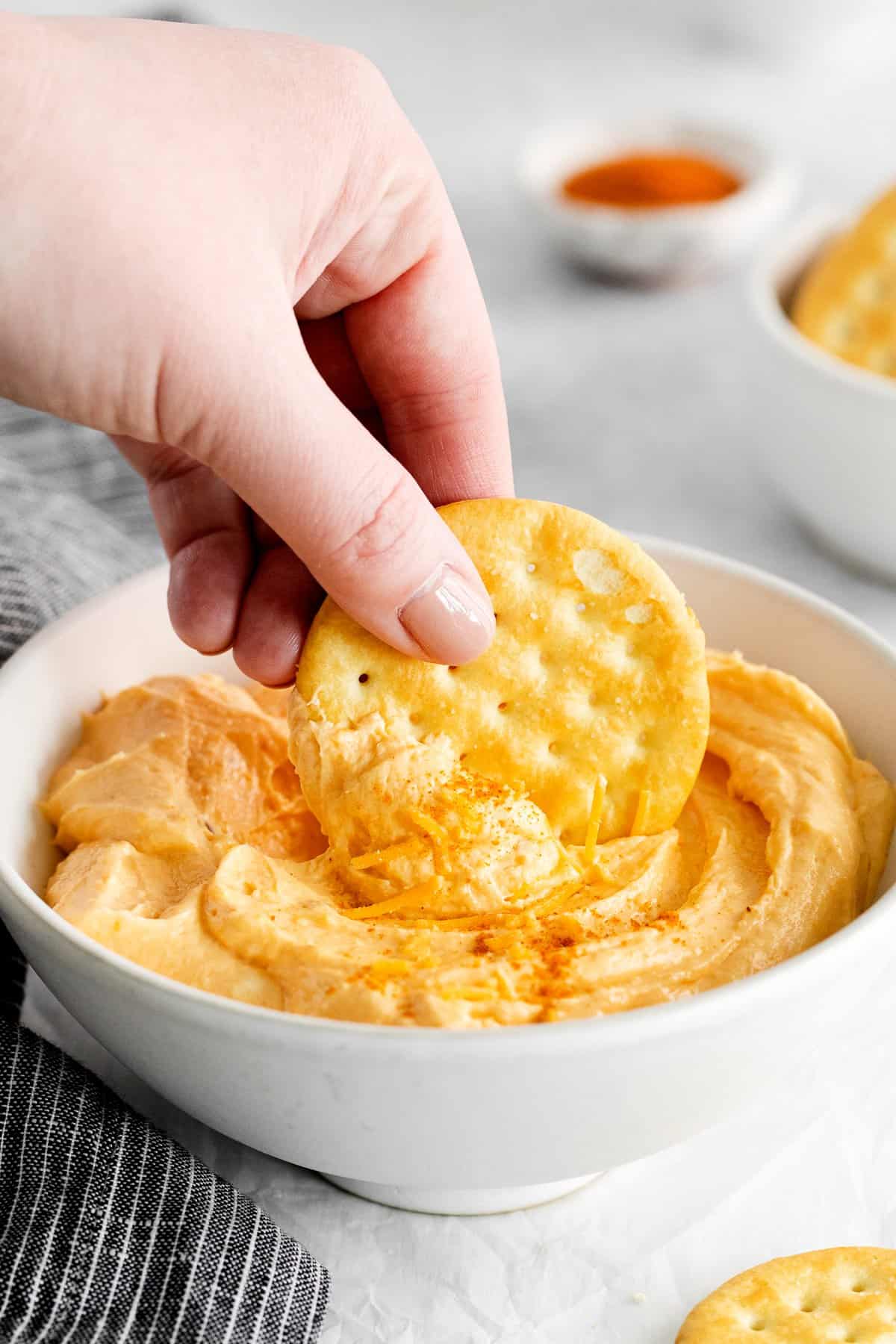 Person dipping a cracker in homemade cheese spread.