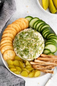 a plate with a cheese ball, crackers and pickles.