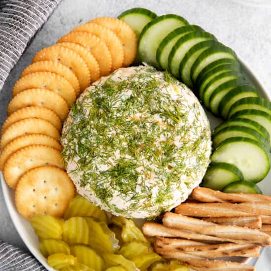 a plate with a cheese ball, crackers and pickles.