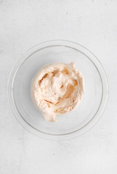 whipped cream in a glass bowl on a white surface.