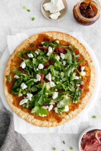 a pizza with arugula and bacon on a white plate.