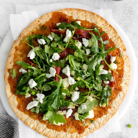 a pizza with arugula and bacon on a white plate.