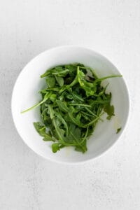 a bowl of arugula on a white surface.