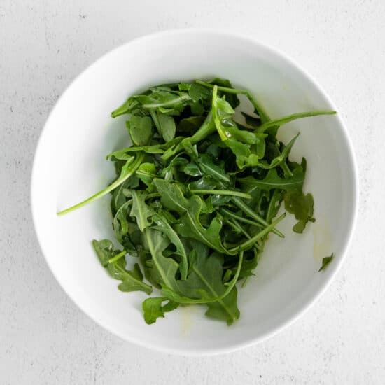 a bowl of arugula on a white surface.
