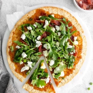 a pizza with greens and bacon on a white plate.