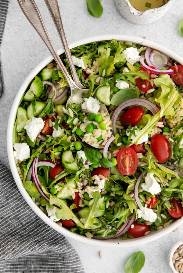 Lemon orzo salad with goat cheese in a salad bowl with serving utensils.